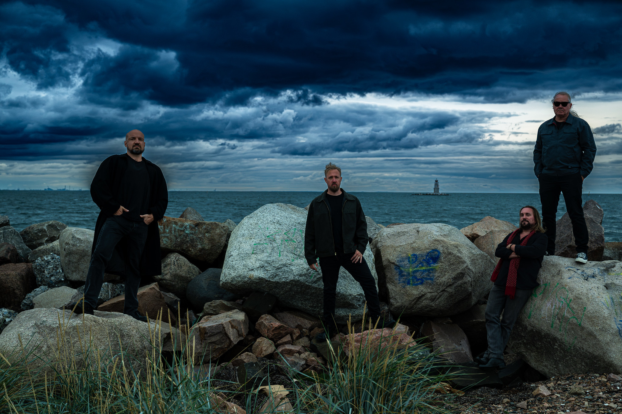The four members of Malsten on a rocky breakwater beneath a towering bank of storm clouds
