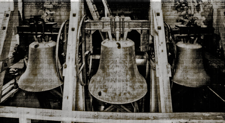 A grainy black-and-white photograph of three large church bells in a wooden belfry frame